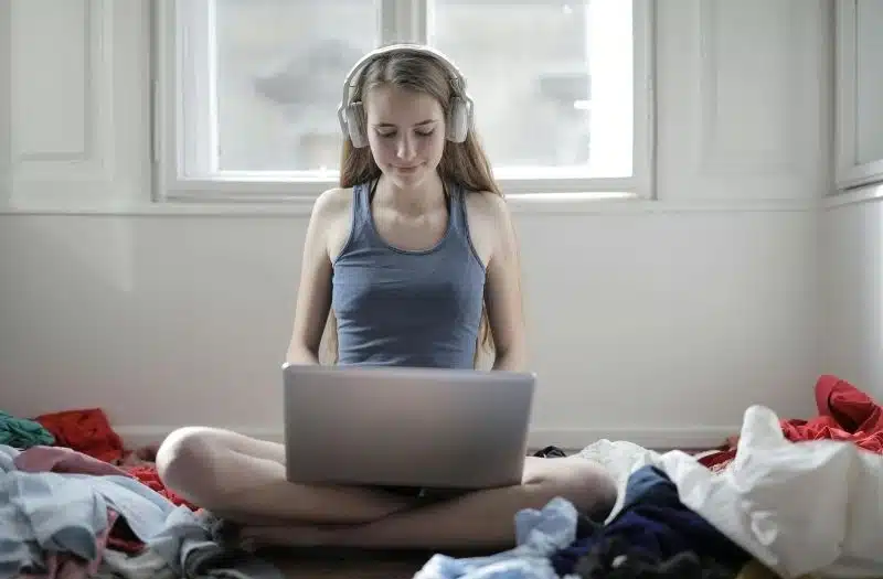 chica joven con auriculares grandes sentada en la cama con el portátil en su regazo escuchandonosla un podcast de cuerpo sexuado
